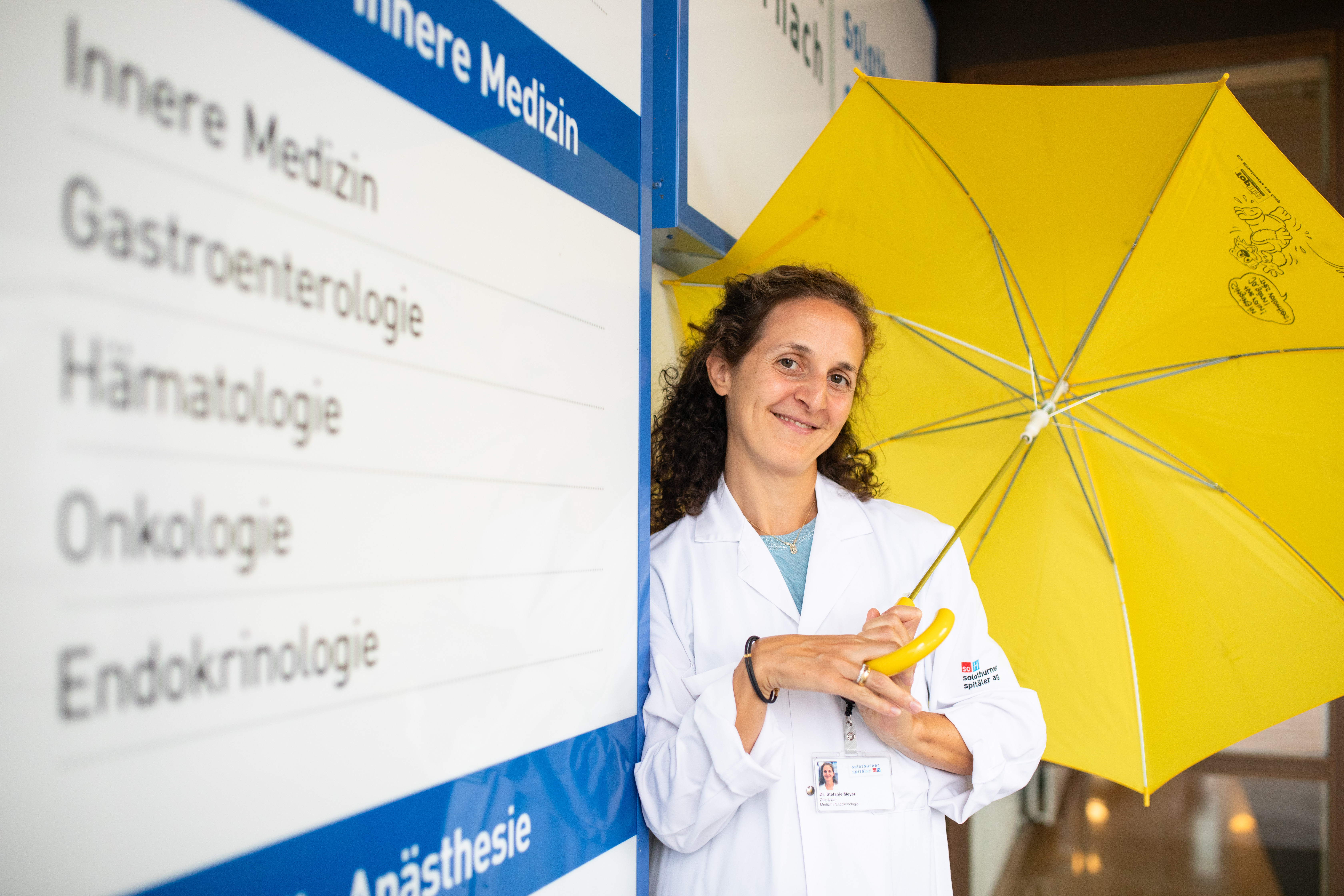 Stephanie Meyer hält einen Regenschirm in der Hand und steht vor dem Eingang des Spitals Dornach