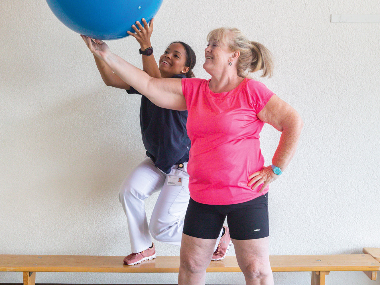 Die Physiotherapeutin und die Patientin bewegen einen Ball in die Höhe.