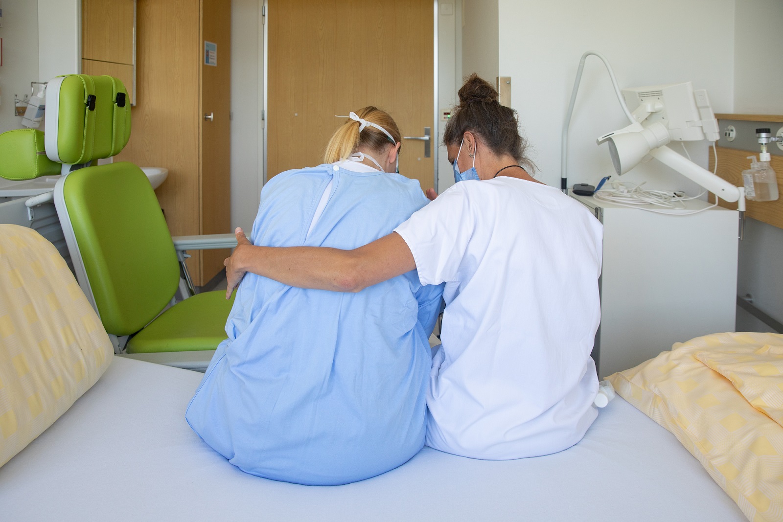 Eine Kinästhetik-Trainerin sitzt neben einer Patientin auf dem Bett