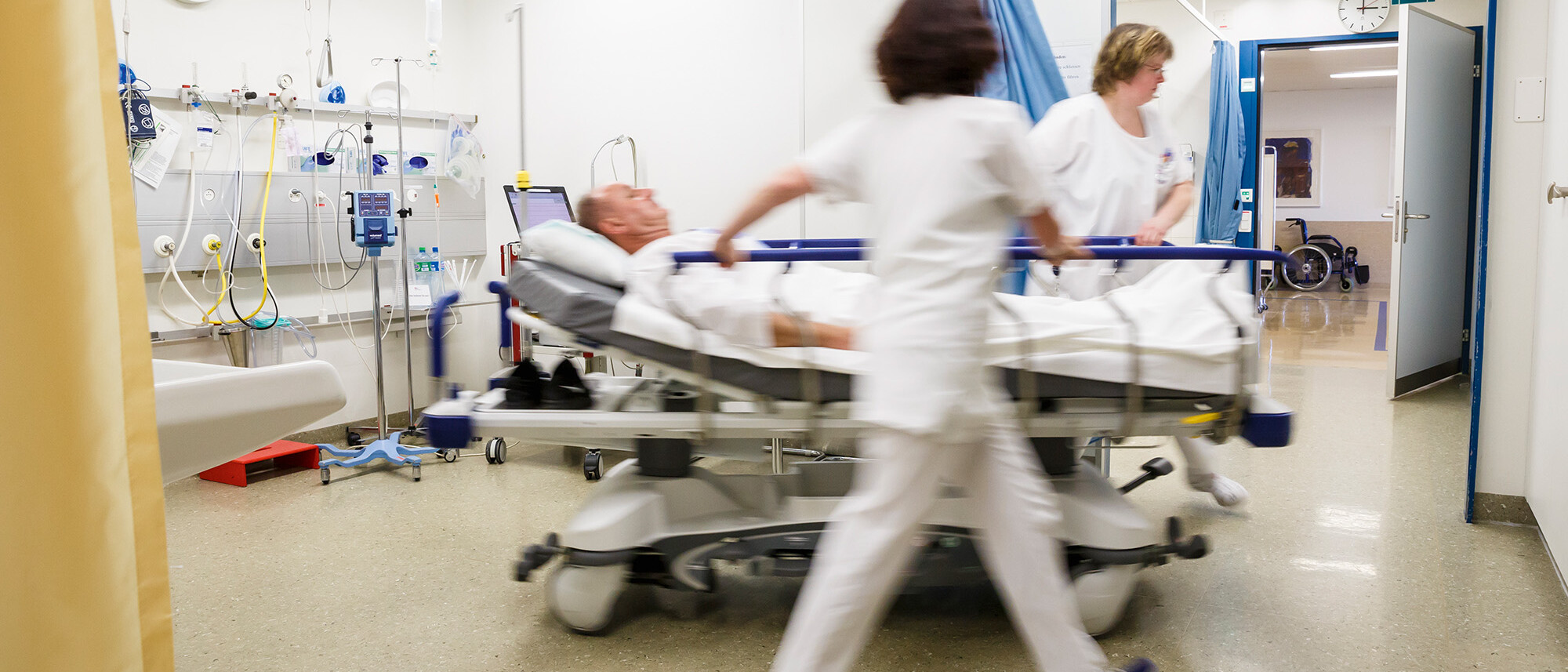 Zwei Pflegerinnen schieben einen Patienten im Bett