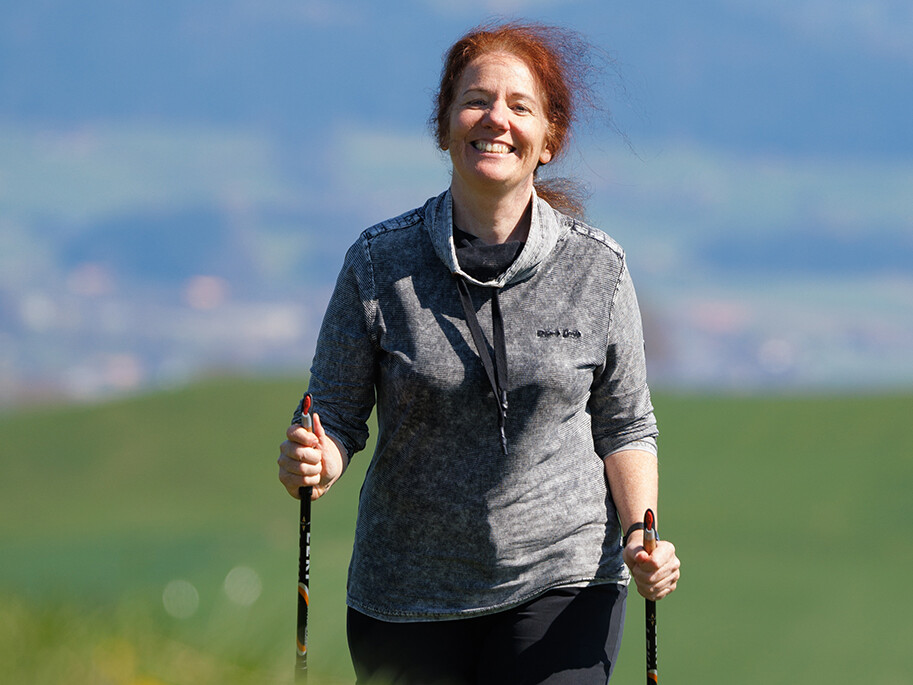 Die Ärztin mit Wanderstöcken auf einer Wiese.