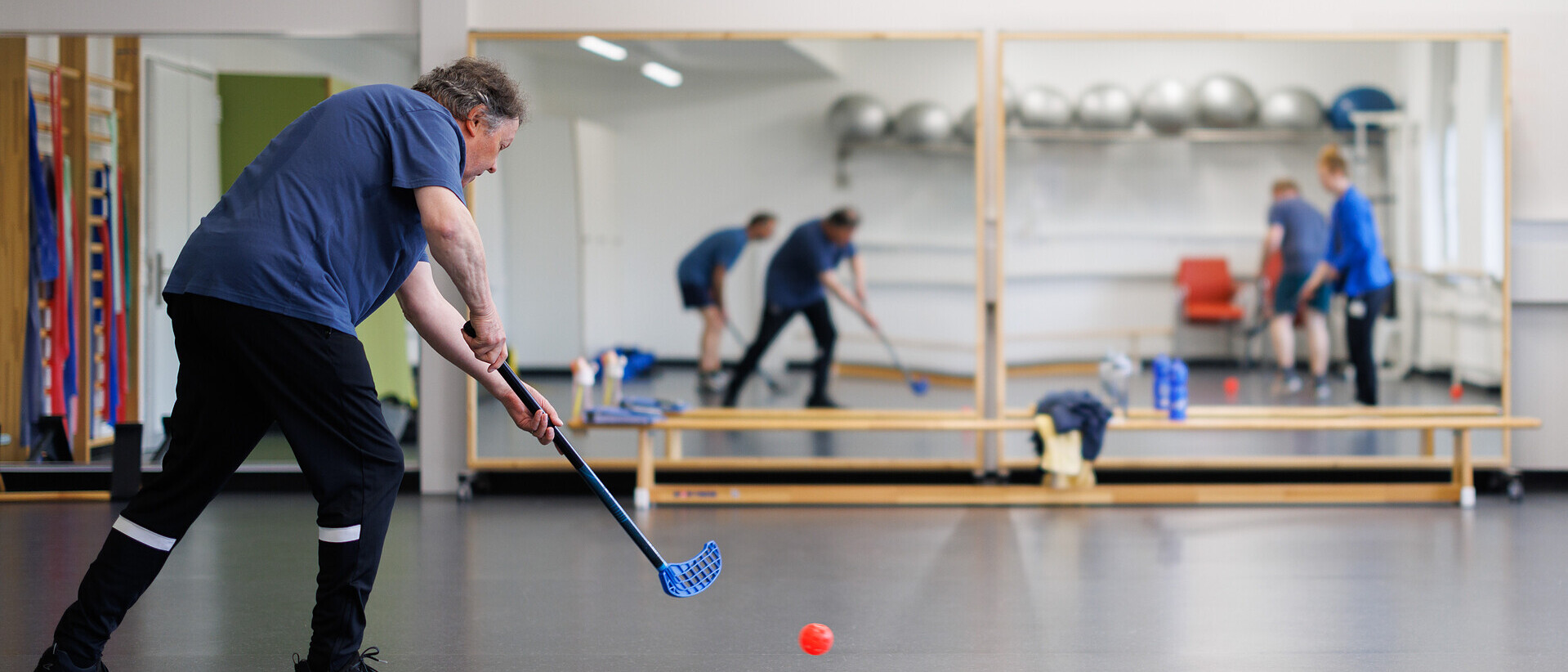 Patient im Sportraum und spielt Unihockey.