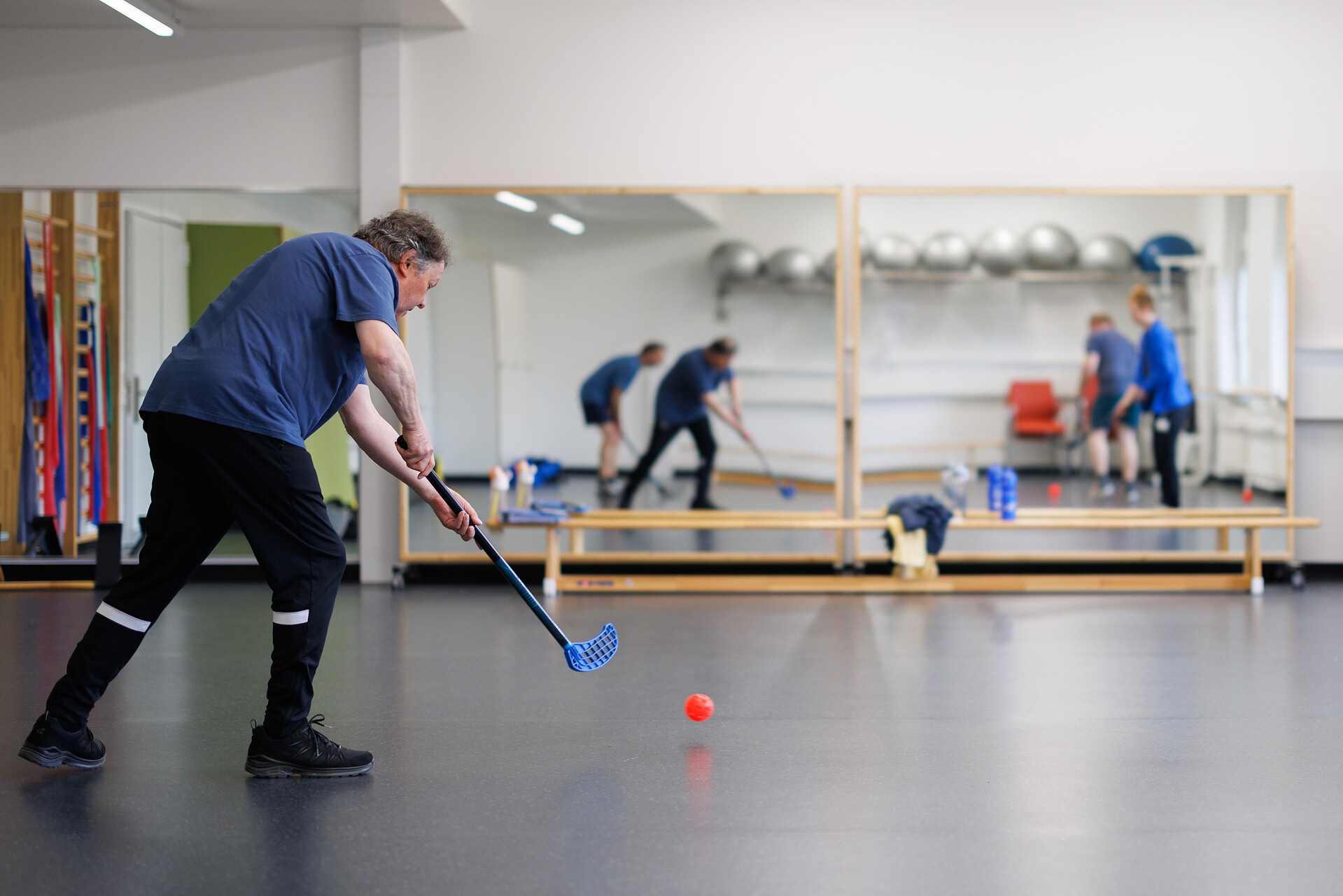 Patient im Sportraum und spielt Unihockey.